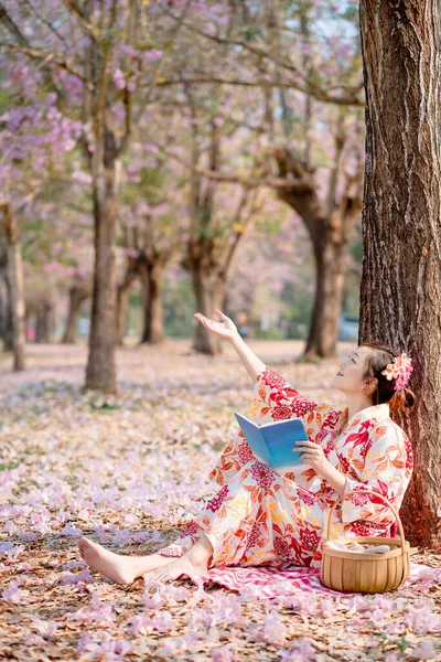 伝統的な着物姿の女性が本を持って春祭りで桜を見て — ストック写真