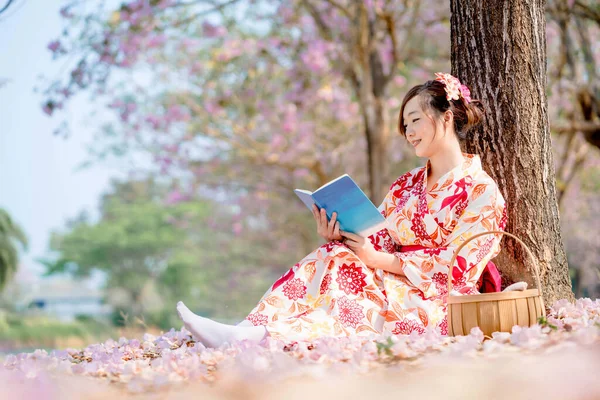 春祭りの桜の本を読む伝統的な着物姿の女性 — ストック写真