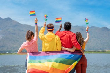 Arkadan bak. Genç çeşitlilik insanları kumsalda gey gururlu gökkuşağı bayrağı ve renkli türbin taşıyor. LGBT topluluğunu destekleyenler 