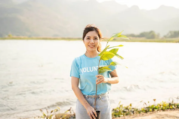 ボランティア女性のポートレート川の上に立ってカメラに笑みを浮かべて緑の植物とポットを保持 環境と自然 生態学的概念の保護 — ストック写真