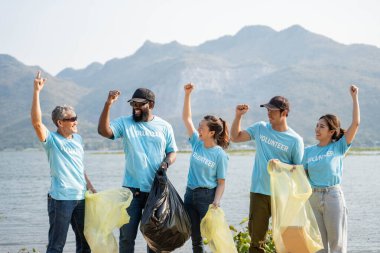 Happy Group of young volunteers helping to keep nature clean and picking up the garbage from a sandy shore. clipart