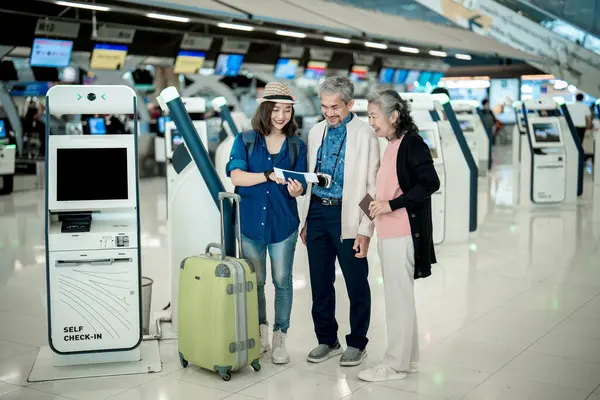 Happy family with young woman checking flight information near self check in machine in international airport.