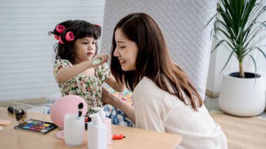 Küçük kız, gülümseyen annesine şakacı bir makyaj yapıyor, sıcak ve sevgi dolu bir aile ortamında evde birlikte vakit geçiriyor..