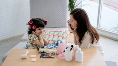 Mutlu bir anne ve kız, makyaj masasında oturup, gülüp kaynaşırken, neşeli bir anın tadını çıkarıyorlar..
