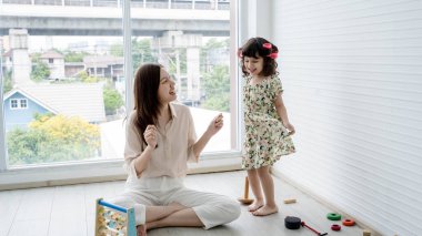 Genç ve mutlu bir anne, evinde kızıyla eğlenirken gülümsüyor ve kaynaşıyor. Aydınlık bir odada eğlenceli aktiviteler yapıyor..