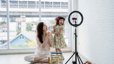 Neşeli anne ve kız dans ediyor ve akıllı telefon ve halka ışığıyla eğlenceli içerikler kaydediyor, rahat bir yaşam alanında birlikte kaliteli zaman geçiriyorlar..