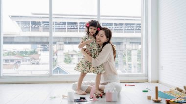 Mutlu bir anne, evinde oyuncaklar ve makyajla çevrili, parlak bir oturma odasında otururken sevgi dolu bir şekilde kızına sarılıyor..