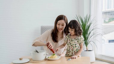 Mutlu anne ve kız spagettiyi evde hazırlayıp çeşnilendiriyorlar. Parlak, rahat bir mutfak ortamında neşeli bir bağ kuruyorlar..