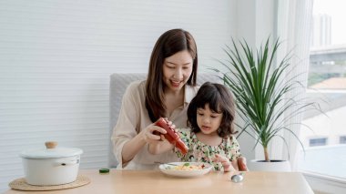 Mutlu anne ve kız spagettiye ketçap ekliyor, ev yapımı sıcak bir mutfakta eğlenceli ve keyifli bir anı paylaşıyorlar..