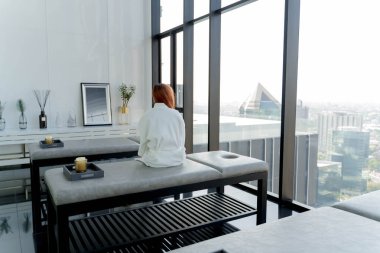Beyaz cüppeli kadın şehir manzaralı modern lüks spa 'da oturuyor. Huzurlu bir huzur ve huzur anı yaşıyor.