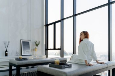 Beyaz cüppeli zarif bir kadın modern lüks bir sağlık merkezinde spa yatağında panoramik şehir manzaralı ve rahatlatıcı bir iç tasarımı olan bir spa yatağında oturuyor.