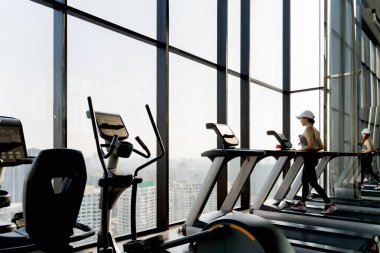 Yüksek katlı spor salonunda panoramik pencere manzaralı koşu bandında yürüyen kadın, modern lüks şehir yaşam tarzında sabah antrenmanı rutini