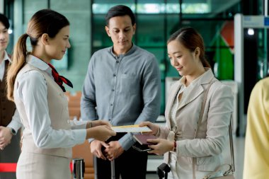 Havaalanı terminalinde kontrol sırasında bayan yolculara uçuş kartı veren gülen havayolu çalışanları, dostça seyahat yardımı sağlıyorlar.