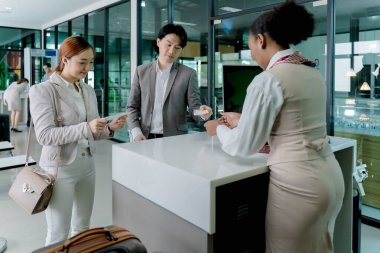 Kayıt gişesinde uçuş kartı sunan iş gezginleri kalkışa hazırlanıyor, havaalanı terminalinde profesyonel personel yardımı yapılıyor.