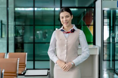 Havaalanının bekleme salonunda duran gülümseyen kadın yer personeli giriş, biniş ve seyahat destek hizmetleri için yolculara yardım etmeye hazır.