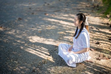 Asyalı kadın bambu gölgeleri altında güneş ışığında meditasyon yapıyor, sessiz bir yolda bacak bacak üstüne atmış, doğada barışı, sükuneti ve farkındalığı kucaklıyor.