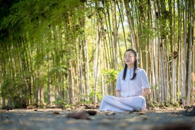 Genç Asyalı kadın sakin bir bambu ormanında huzur içinde meditasyon yapıyor, gözleri kapalı, doğal çevrede farkındalığı ve manevi huzuru kucaklıyor.
