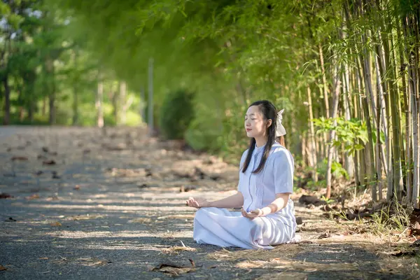 Sessiz, bambu kaplı bir yolda oturmuş meditasyon yapan bir kadın, huzurlu doğal orman ortamında iç huzurunu ve farkındalığını buluyor.