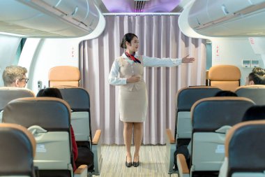 Uzman uçuş görevlisi, inflight güvenlik gösterileri sırasında acil çıkışları işaret ederek, yolcuların uçaklardaki tahliye prosedürlerinden haberdar olmalarını sağlar.