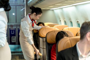 Uçuş görevlisi yolcu kabininde yolculara yardım ediyor, koltuğu ayarlıyor ve ticari bir havayolu seyahatine çıkmadan önce konfor ve güvenliği sağlıyor.