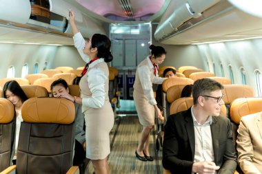 Kabin personeli yolculara yardım ediyor ve ticari uçuş sırasında bavulları güvence altına alıyor, modern uçak kabin ortamında güvenliği ve konforu sağlıyor