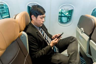 Resmi takım elbiseli iş adamı uçak penceresinin yanında otururken akıllı telefon kullanıyor, uçuş sırasında ekrana odaklanıyor, modern uçuş bağlantısı kavramı