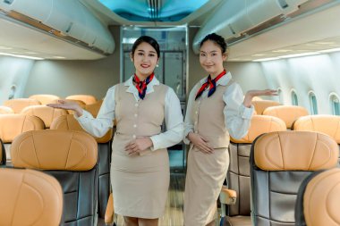 Profesyonel uçuş görevlileri uçakta yolcuları karşılıyor, dostça gülümsemelerle uçak koridorunda duruyorlar, olağanüstü bir hizmet ve konukseverlik sunuyorlar.