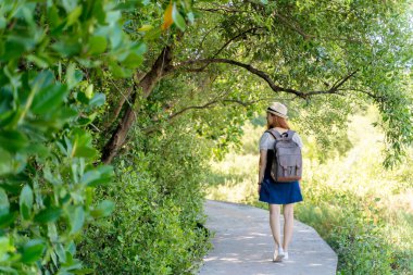 Yaz günlerinde yemyeşil bir ormanda gezen, sırt çantası ve şapka takan, barışçıl yalnız doğa keşiflerinin tadını çıkaran genç bir kadın..
