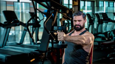 Güçlü, olgun bir adam spor salonunda halter egzersizine konsantre oluyor. Sağlıklı yaşam tarzına yoğun odaklanma ve adanmışlıkla kas geliştiriyor.