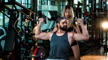Spor salonunda halterleri kaldıran kaslı bir adama yardım eden kişisel antrenör, sağlıklı yaşam tarzı için kas geliştirme, kas geliştirme ve fitness koçluğu üzerine odaklanmış..