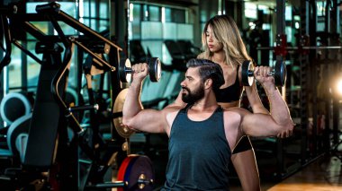 Spor salonunda dambılları kaldıran, kas geliştirmeye odaklanan ve spor ve sağlık gelişimi için rehberlik eden kişisel antrenör..