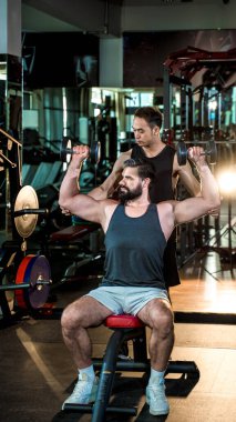 Spor salonunda halterli omuz egzersizi yapan kişisel antrenör kas geliştirme, güç eğitimi ve fitness motivasyonuna odaklanıyor..