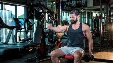 Spor salonunda dambıllarla antrenman yapan kararlı olgun bir adam. Sağlıklı yaşam tarzı ve fitness hedefleri için kas geliştirmeye odaklanıyor.