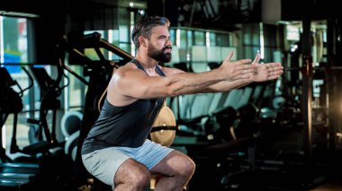 Odaklanmış kaslı adam spor salonunda çömelme egzersizi yapıyor. Egzersiz sırasında güç ve denge gösteriyor. Mükemmel formda.
