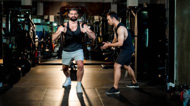 Güçlü bir adam, profesyonel bir spor salonunda spor salonundaki spor eğitmeninin rehberliğinde hareket eder. Güç, form ve dayanıklılık üzerine odaklanır..