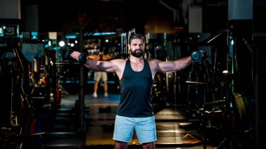 Odaklanmış bir adam spor salonunda antreman yapıyor, vücudunun üst kısmını gösteriyor, kas kontrolü ve kendini karanlık, profesyonel bir ortama adamış..