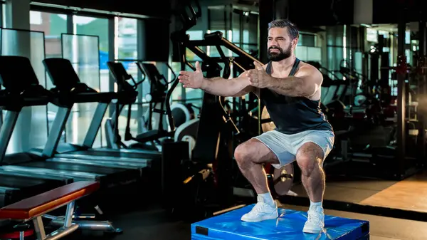 Modern spor salonundaki yumuşak kutunun üzerinde plyometrik hareketler yapan odaklanmış bir adam işlevsel antrenman sırasında güç, denge ve düzgün bir form sergiliyor..