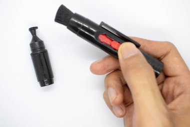 Elinde bir mercek tutuyordu, beyaz arka planda kamera lenslerini temizlemek için özel bir fırça.