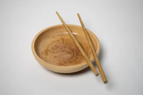 Bir çift ahşap çubuk yuvarlak bir ahşap kasede duruyor, minimalist doğal sofra takımı sergileniyor..