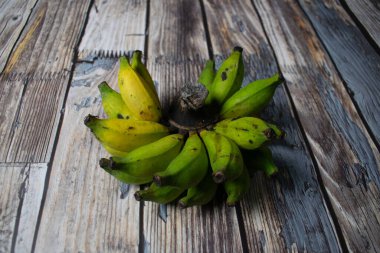 Bir demet olgunlaşmamış ve yarı olgunlaşmamış muz rustik ahşap tahtalarda dizilmiş..