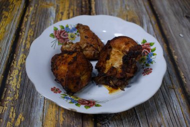 Kırsal ahşap bir masanın üzerinde eski bir çiçek tabağında servis edilen kızarmış tavuk parçaları..