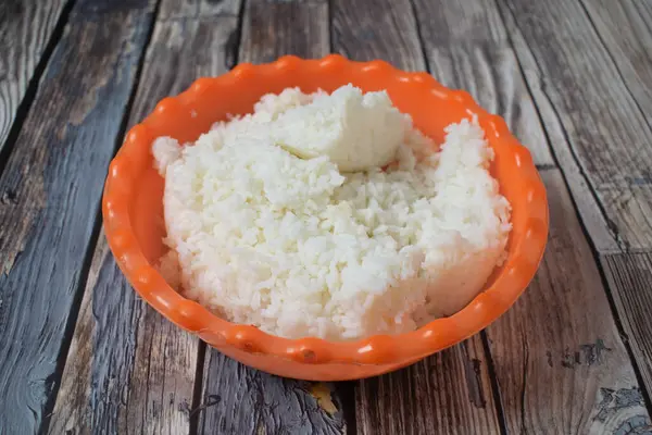 Kırsal bir masada parlak turuncu bir kasede servis edilen buğulanmış beyaz pirinç..