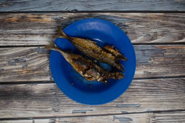 Geleneksel kızarmış balık, canlı mavi bir tabakta köy ortamında servis edilir.