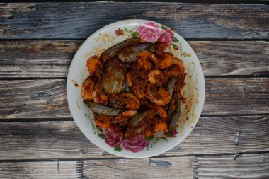 Patlıcan ve baharatlı karides kırsal bir ahşap masada çiçek desenli bir kasede servis edilir..