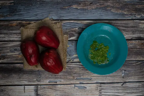 Kırsal ahşap yüzeyde yeşil biber sosuyla servis edilen taze kırmızı guava.