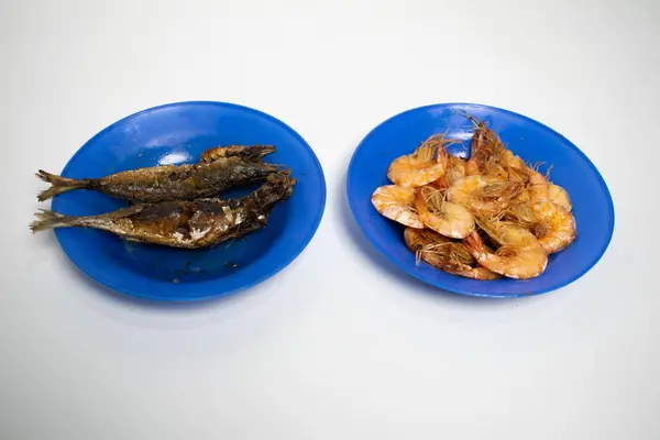 İki parlak mavi tabak klasik deniz ürünleri tabağı ve kıtır beyaz arka planda servis edilen kızarmış balık ve lezzetli karides içerir..