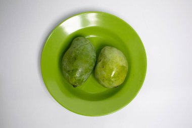 Benzer yeşil bir tabakta, temiz beyaz bir yüzeye yerleştirilmiş iki taze mango..