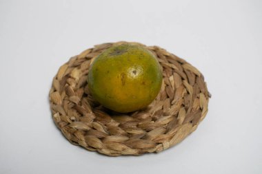 Taze yeşil-turuncu portakallar, beyaz arkaplan ile dokunmuş bir hasırın üzerine yerleştirilir..