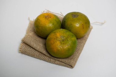 Katlanmış bir çuval bezi üzerine üç taze portakal konur, kırsal ve doğal bir his verir..