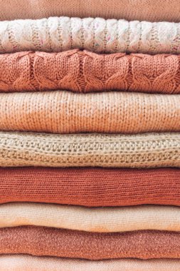 Neat stack of woolen sweaters in pastel beige, pink and orange tones. Autumn and winter fashion aesthetic. Textured wool background.